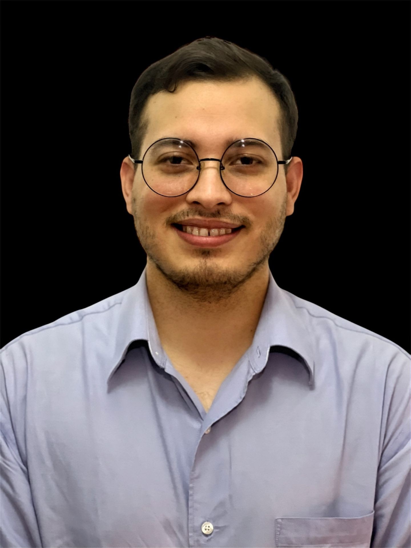 Man wearing glasses and a light blue shirt, smiling with a black background.