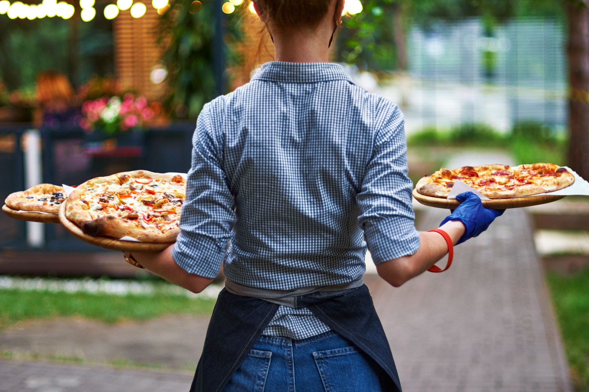 Girl waiter with her back to us with three birds in her hands on the restaurant terrace