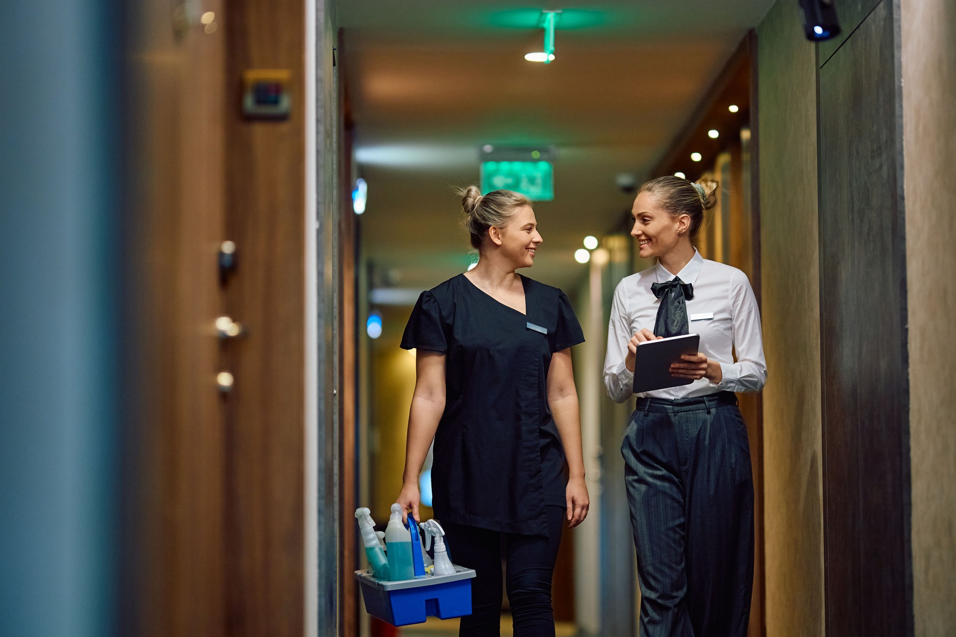 Happy hotel maid talking to housekeeping manager while waking through hallway,